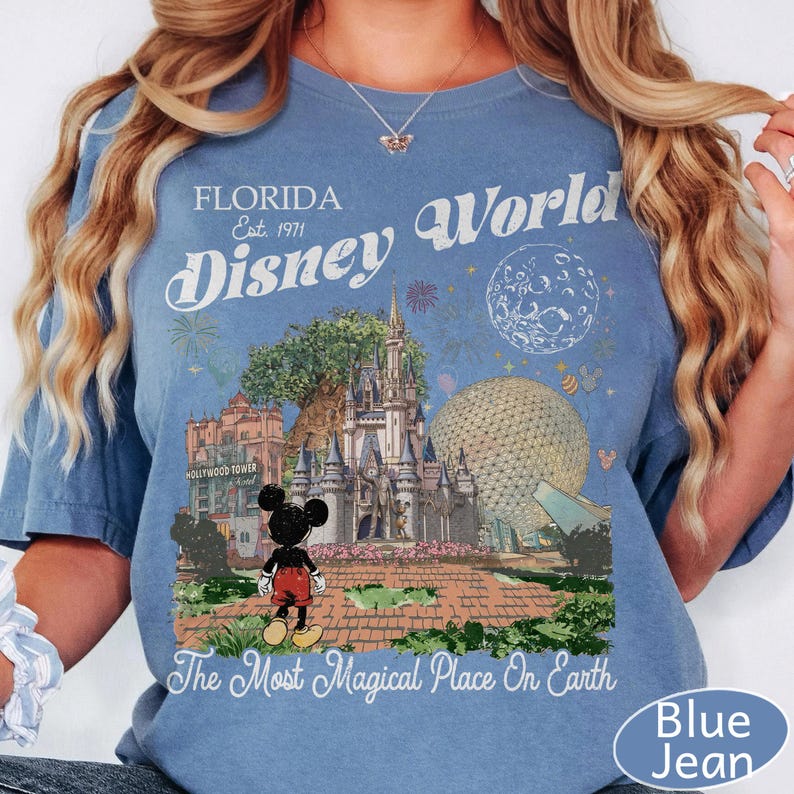 K&ouml;nnte beinhalten: Ein blaues T-Shirt mit einem Grafikdruck von Florida Disney World, einschlie&szlig;lich Schloss, Epcot-Sph&auml;re, Hollywood Tower Hotel und Mickey Mouse. Der Text lautet Florida Est. 1971, Disney World und The Most Magical Place On Earth.