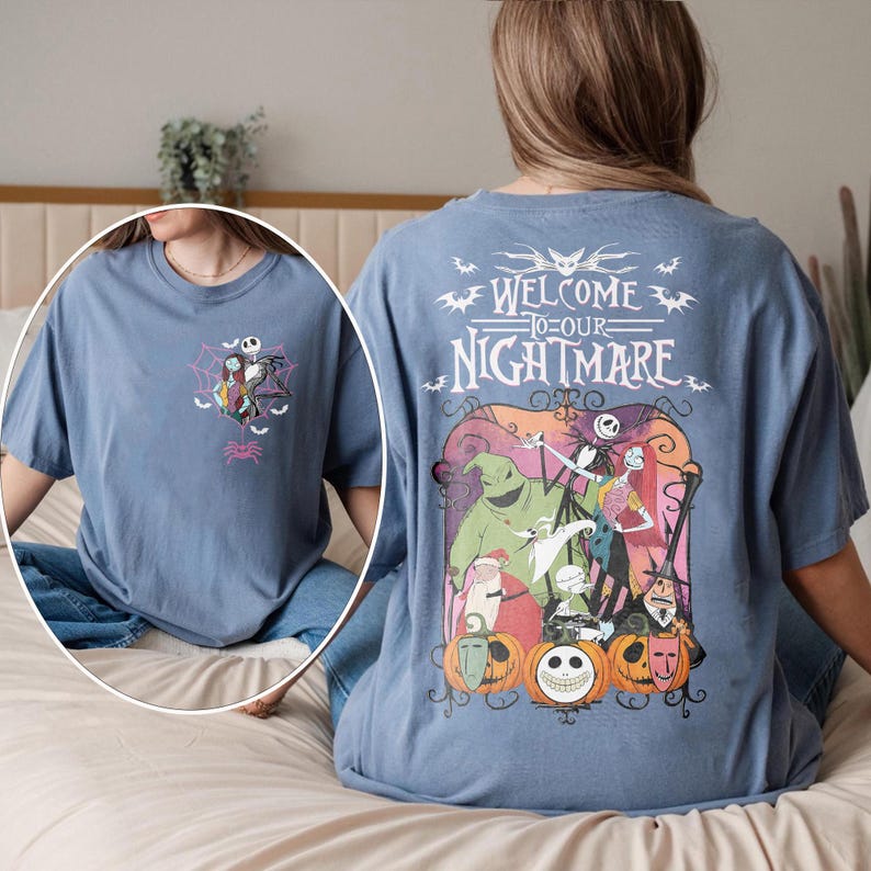 May include: A blue t-shirt featuring a graphic from "The Nightmare Before Christmas." The front has a small design with Jack Skellington and Sally. The back displays the phrase "Welcome to Our Nightmare" with various characters and pumpkins.