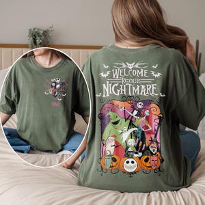 May include: Olive green t-shirt featuring a graphic from "The Nightmare Before Christmas." The front has a small design of Jack Skellington and Sally in a spiderweb. The back has the text "Welcome to our Nightmare" with characters and pumpkins.
