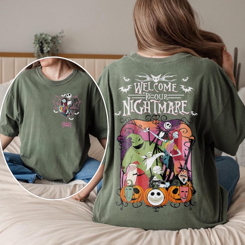 May include: Olive green t-shirt featuring a graphic from "The Nightmare Before Christmas." The front has a small design of Jack Skellington and Sally in a spiderweb. The back has the text "Welcome to our Nightmare" with characters and pumpkins.