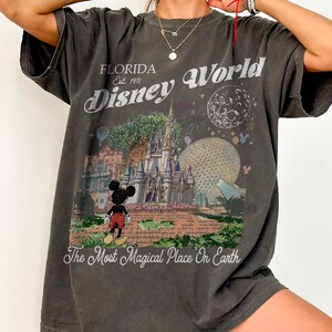 K&ouml;nnte beinhalten: Ein anthrazitfarbenes Kurzarm-T-Shirt mit einem Grafikdruck des Disney World Schlosses, der Epcot-Kugel und Mickey Mouse. Der Text lautet Florida Est. 1971 Disney World und The Most Magical Place On Earth in einer wei&szlig;en Vintage-Schrift.