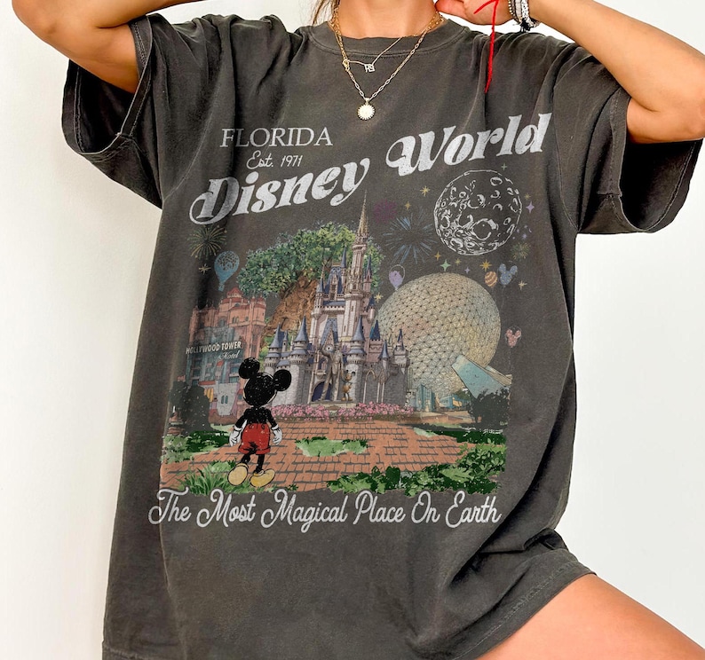 K&ouml;nnte beinhalten: Ein anthrazitfarbenes Kurzarm-T-Shirt mit einem Grafikdruck des Disney World Schlosses, der Epcot-Kugel und Mickey Mouse. Der Text lautet Florida Est. 1971 Disney World und The Most Magical Place On Earth in einer wei&szlig;en Vintage-Schrift.