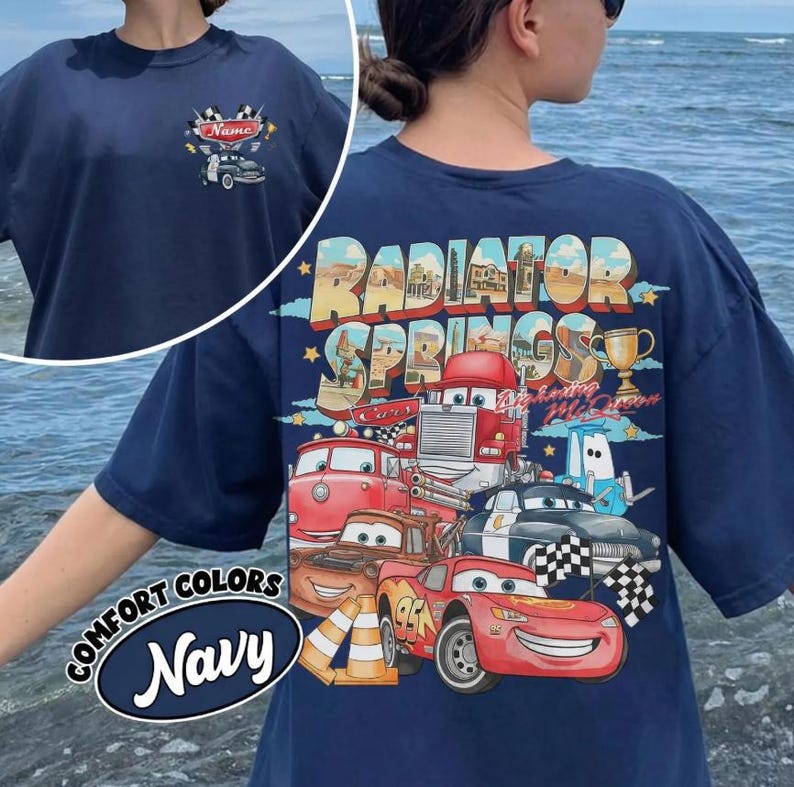May include: Navy blue t-shirt featuring a graphic of various cartoon cars with the text "Radiator Springs" on the back. The front of the shirt has a small car graphic and the word "Name". The shirt also has the words "Comfort Colors Navy".