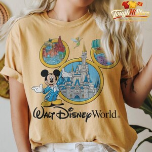 May include: Mustard yellow t-shirt featuring Mickey Mouse in a blue suit, with the text "Walt Disney World." The shirt has a graphic of the Disney World castle and other park attractions. The shirt is a comfortable, casual style.