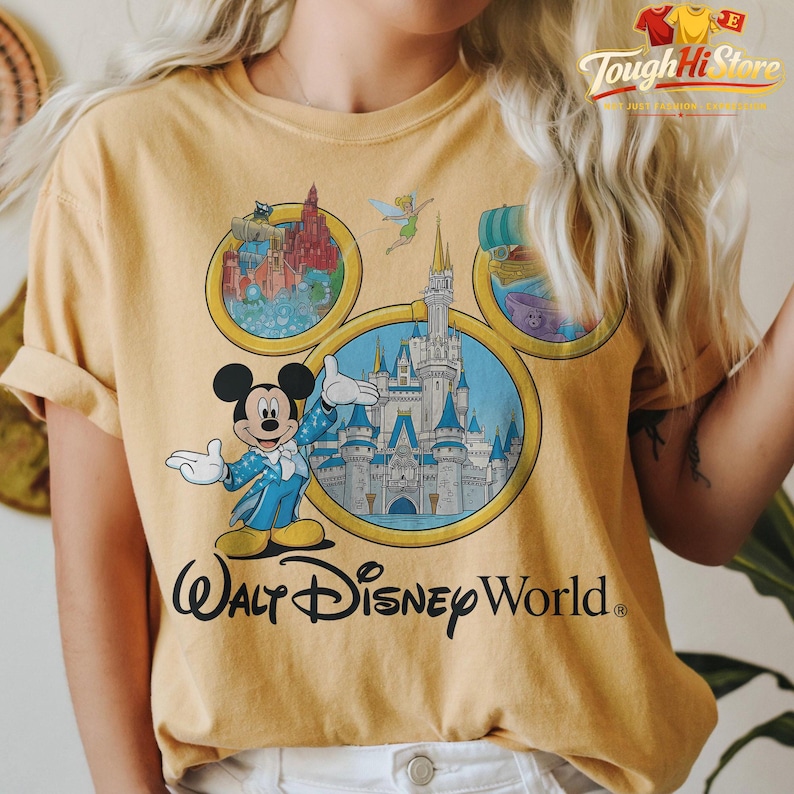 May include: Mustard yellow t-shirt featuring Mickey Mouse in a blue suit, with the text "Walt Disney World." The shirt has a graphic of the Disney World castle and other park attractions. The shirt is a comfortable, casual style.