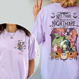 May include: A light purple t-shirt featuring a graphic from "The Nightmare Before Christmas." The front has a small design of Jack and Sally. The back has a larger design with the text "Welcome to our Nightmare" and characters from the movie.