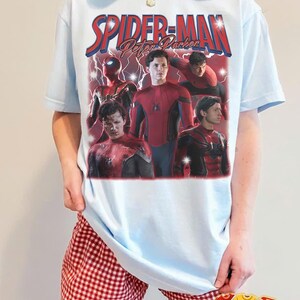 May include: Light blue t-shirt featuring a graphic of Spider-Man with the text "Spider-Man Peter Parker". The design includes multiple images of Spider-Man in his suit. The shirt is a light blue color.