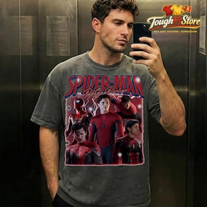 May include: Gray t-shirt featuring a graphic of Spider-Man and the text "Spider-Man Peter Parker" in red and blue. The shirt has a vintage style and a distressed look. The image on the shirt includes multiple images of Spider-Man.
