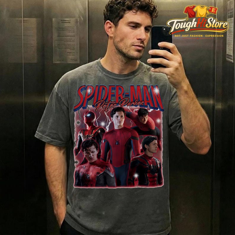 May include: Gray t-shirt featuring a graphic of Spider-Man and the text "Spider-Man Peter Parker" in red and blue. The shirt has a vintage style and a distressed look. The image on the shirt includes multiple images of Spider-Man.