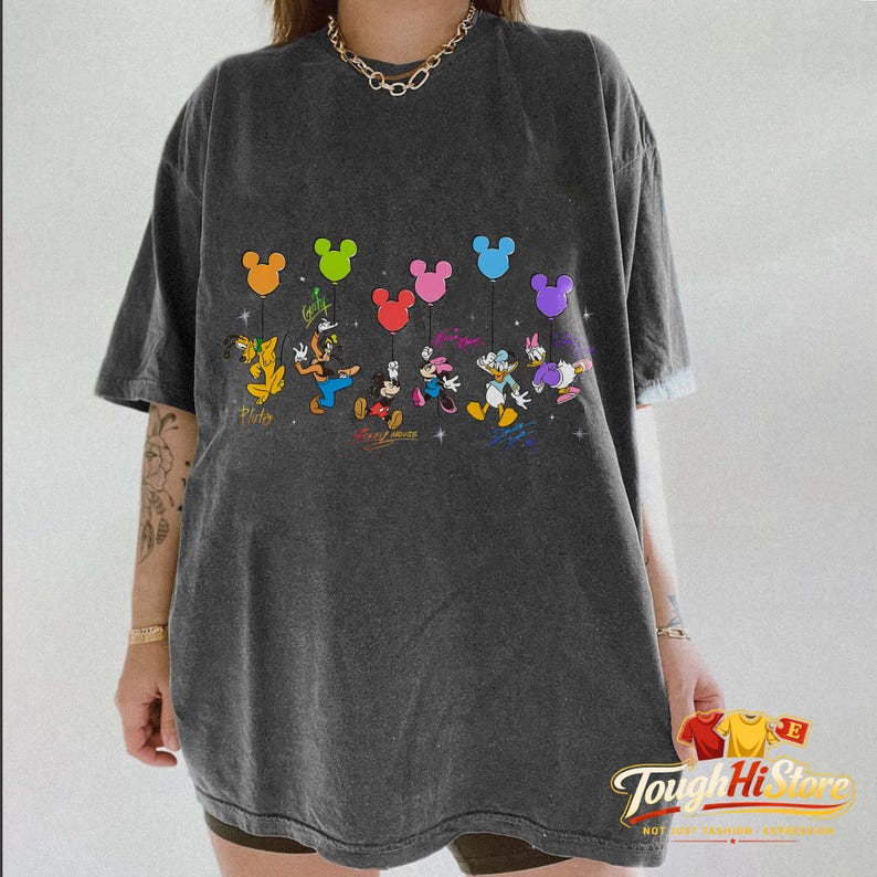 May include: Dark gray t-shirt featuring a colorful graphic of Disney characters holding Mickey Mouse-shaped balloons. The design includes Pluto, Goofy, Mickey, Minnie, Donald, and Daisy. The text "Disney Forever" is also included.