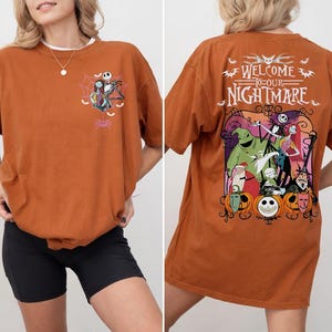 May include: Rust-colored t-shirt featuring a graphic from "The Nightmare Before Christmas." The front has a small design of Jack Skellington and Sally. The back displays a larger, colorful scene with the text "Welcome to our Nightmare."