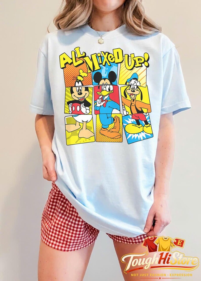 Puede incluir: Camiseta azul claro con un gr&aacute;fico colorido de Mickey Mouse, el Pato Donald y Goofy con el texto "ALL MIXED UP!". El dise&ntilde;o es de estilo c&oacute;mic. Una prenda de vestir informal.