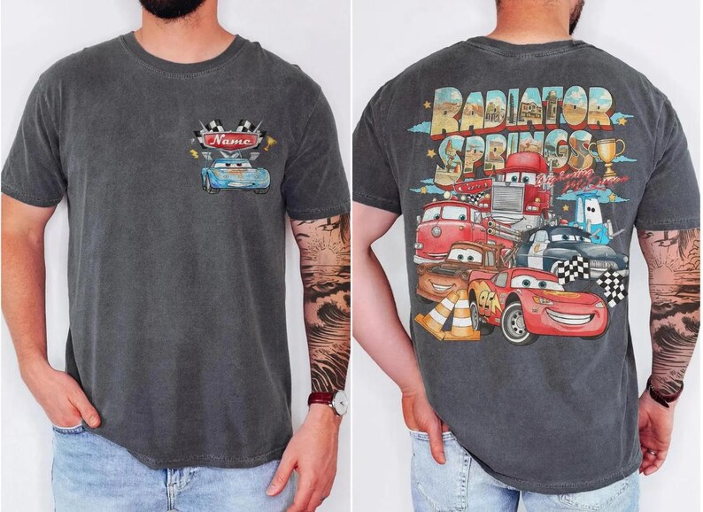 May include: Charcoal gray t-shirt featuring a cartoon car design on the front with the word "Name" above it. The back of the shirt displays a colorful graphic of various cartoon cars with the text "Radiator Springs".