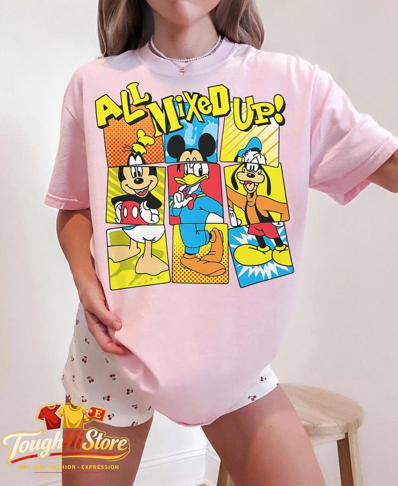 Puede incluir: Camiseta rosa claro con un dise&ntilde;o de c&oacute;mic de Mickey, Donald y Goofy, con el texto "ALL MIXED UP!". El dise&ntilde;o utiliza colores brillantes y contornos. Parte de una colecci&oacute;n de ropa.