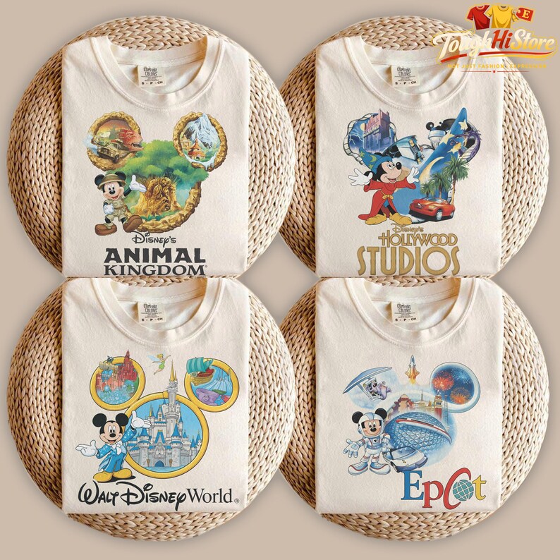 May include: Four cream-colored t-shirts with Disney character designs. Each shirt features a different Disney theme: Animal Kingdom, Hollywood Studios, Walt Disney World, and Epcot. The shirts are arranged on a woven surface.