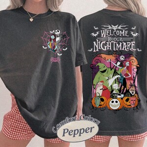 May include: Dark gray t-shirt featuring characters from The Nightmare Before Christmas. The front has Jack and Sally in a web, and the back says "Welcome to our Nightmare" with other characters and pumpkins. The shirt is a Comfort Colors Pepper.