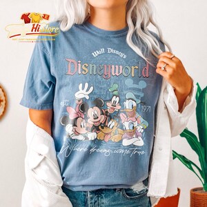 Puede incluir: Camiseta azul con la inscripci&oacute;n "Walt Disney's Disneyworld" y el a&ntilde;o "1971". La camiseta presenta un gr&aacute;fico de personajes de Disney, incluyendo Mickey Mouse, Minnie Mouse, Donald Duck y Goofy, con la frase "Where dreams come true."