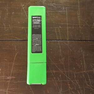 May include: A vivid green rectangular case with a black label. The label displays the text "E7018AC" and technical details. The case is placed on a dark wooden surface.