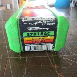 May include: A green and black package of Forney E7018AC welding rods. The label includes the size 5/32" (4.6mm) and weight 5 lbs. (2.27Kg). The package is marked "MADE IN MEXICO".