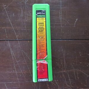 May include: A green rectangular package of E7018AC premium electrodes, 5 lbs (2.27kg). The package has a yellow and red label with text in English and Spanish. The package is on a dark brown wooden surface.