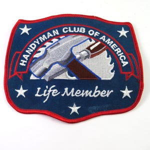 May include: A navy blue patch with a red border features the text "Handyman Club of America" and "Life Member". The patch includes a silver hammer and saw design, along with white stars.
