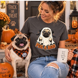 May include: A dark grey short-sleeve t-shirt featuring a graphic of a pug wearing a white ghost sheet with the text PUG A BOO in orange letters, accompanied by small black bat illustrations and orange star accents on the front of the garment.