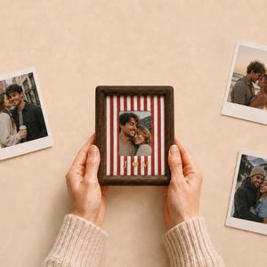 Peut inclure: Un cadre photo en bois foncé contenant une photo de couple, sur un fond à rayures verticales rouges et blanches avec les lettres dorées J et M séparées par un cœur. Trois autres photos de style polaroïd de couples sont disposées à proximité.