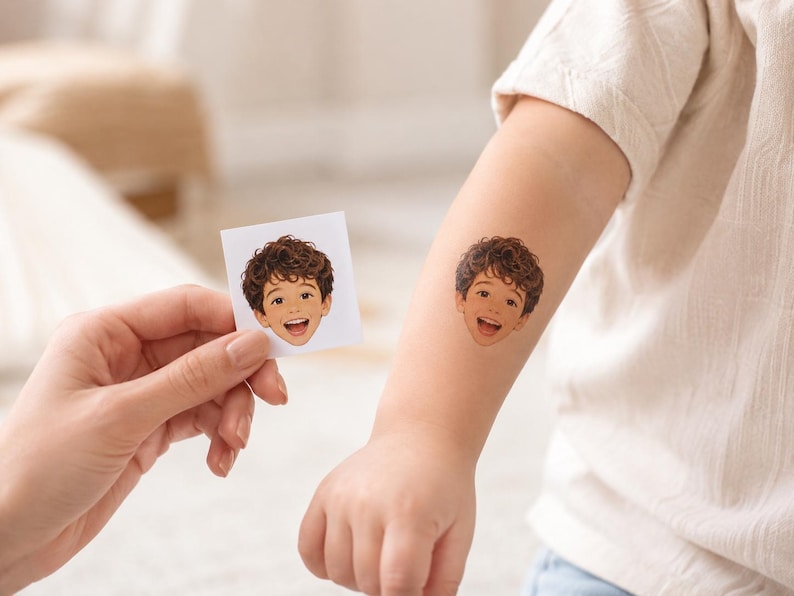 May include: A square white paper sheet featuring a colorful illustration of a smiling child with curly brown hair, alongside a matching temporary tattoo applied to an arm, depicting the same illustration of the child's face with a joyful expression.