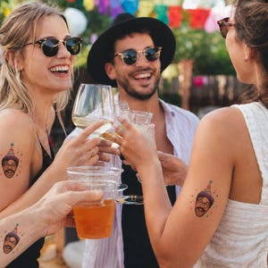 May include: Temporary tattoos featuring a cartoon face wearing a colorful party hat. The design includes a smiling person with glasses and a mustache, topped with a multi-colored cone hat, applied to the skin of three different individuals.