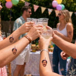 May include: Temporary tattoos applied to the skin of three individuals, each featuring a colorful illustration of a person wearing a party hat. The design depicts a smiling face with glasses and a multi-colored cone-shaped hat with a pom-pom on top.