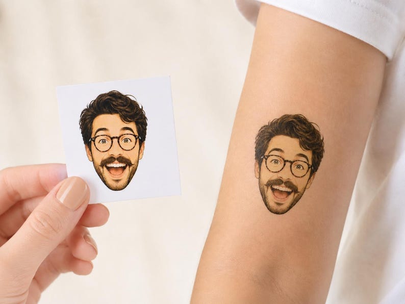 May include: A temporary tattoo featuring a cartoon-style illustration of a person with dark wavy hair, a mustache, and round glasses, shown with a wide, happy expression. The same illustration is displayed on a square white paper backing.