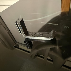 May include: A black 3D printed L-shaped bracket with a textured surface. The horizontal section features the embossed text LY 3D. The object has a vertical arm and a base designed for mounting or support, showing clear layer lines from the printing process.