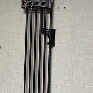 May include: A black and gray camouflage-patterned bow quiver with six black arrows. The quiver is mounted on a wall and features a black mounting bracket. The arrows are held in place by a series of black tubes.