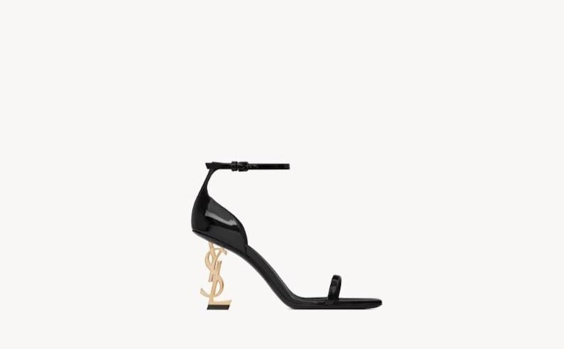 Puede incluir: Sandalia de charol negro con tac&oacute;n dorado en forma de letras YSL. La sandalia presenta una fina correa en el tobillo y una correa individual en la puntera. La altura del tac&oacute;n es de unos 10 cm.
