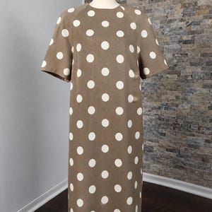 May include: A knee-length dress in a muted brown color featuring a repeating pattern of large, circular white polka dots. The garment has short sleeves, a round neckline, and a straight, shift-style silhouette displayed on a mannequin.