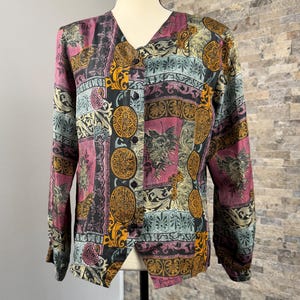 May include: A long-sleeved button-down shirt featuring a multi-colored patchwork pattern in shades of magenta, gold, black, and teal. The design includes intricate floral motifs, paisley shapes, and circular medallions across the entire garment.