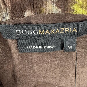 May include: Close-up of a brown garment with a floral pattern. The label reads "BCBGMAXAZRIA", "MADE IN CHINA", and size "M". The fabric has a textured appearance.