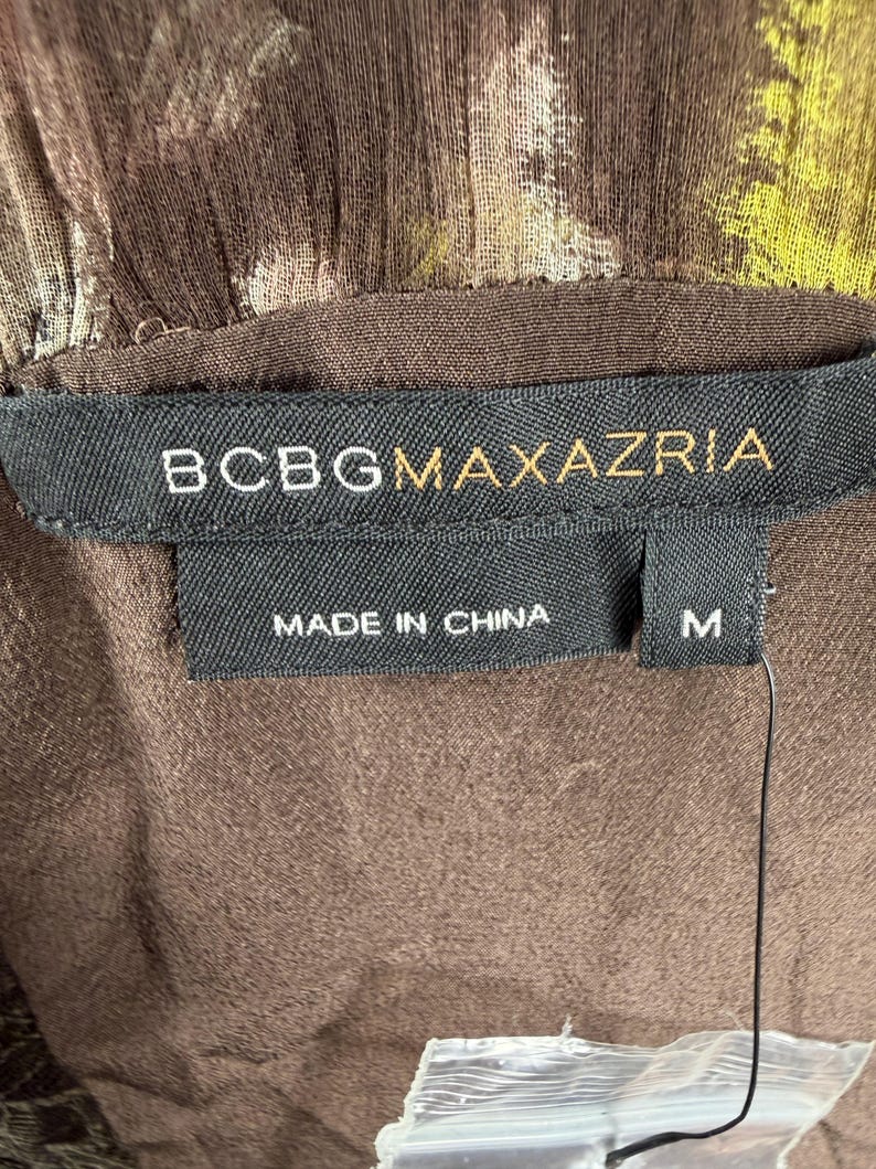 May include: Close-up of a brown garment with a floral pattern. The label reads "BCBGMAXAZRIA", "MADE IN CHINA", and size "M". The fabric has a textured appearance.