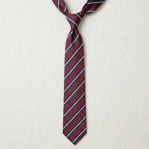 May include: A burgundy tie with white and navy blue stripes. The tie is knotted at the top, with the striped pattern running vertically down the length of the tie. The background is a neutral off-white color.