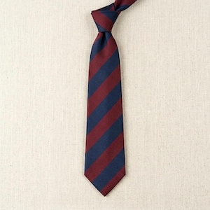 Peut inclure: Une cravate rayée bleu marine et bordeaux. Le nœud est fait en haut, et les rayures courent verticalement sur toute la longueur. Le fond est un tissu neutre et texturé. Un accessoire classique.
