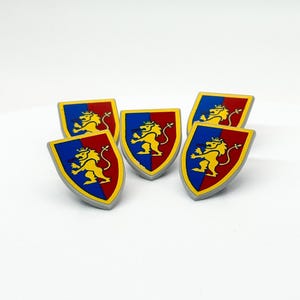 Puede incluir: Cinco escudos en forma de escudo con un león amarillo rampante sobre un fondo rojo y azul. Los escudos tienen un borde dorado y están dispuestos sobre una superficie blanca. El león está coronado y tiene una larga cola.