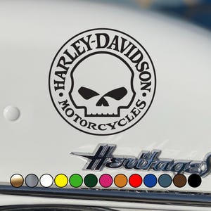 May include: Black Harley-Davidson Motorcycles skull logo sticker. The circular design features a skull graphic and the brand name. The sticker is displayed on a white surface, with a row of color options below.