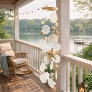 May include: A coastal-themed wind chime with a wooden ring and starfish accent. The chime features translucent, round shell discs and wooden beads, creating a gentle, decorative hanging ornament. The background shows a porch overlooking a lake.
