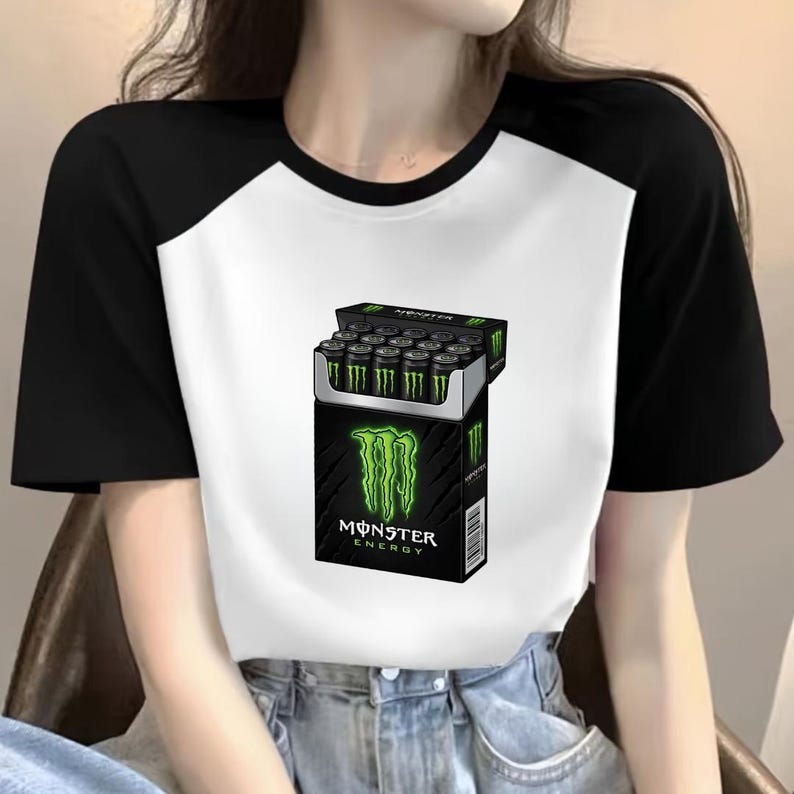 May include: A white t-shirt with black raglan sleeves featuring a graphic print of a cigarette pack filled with green and black Monster Energy drink cans. The black box displays the green Monster logo and the text Monster Energy in white letters.