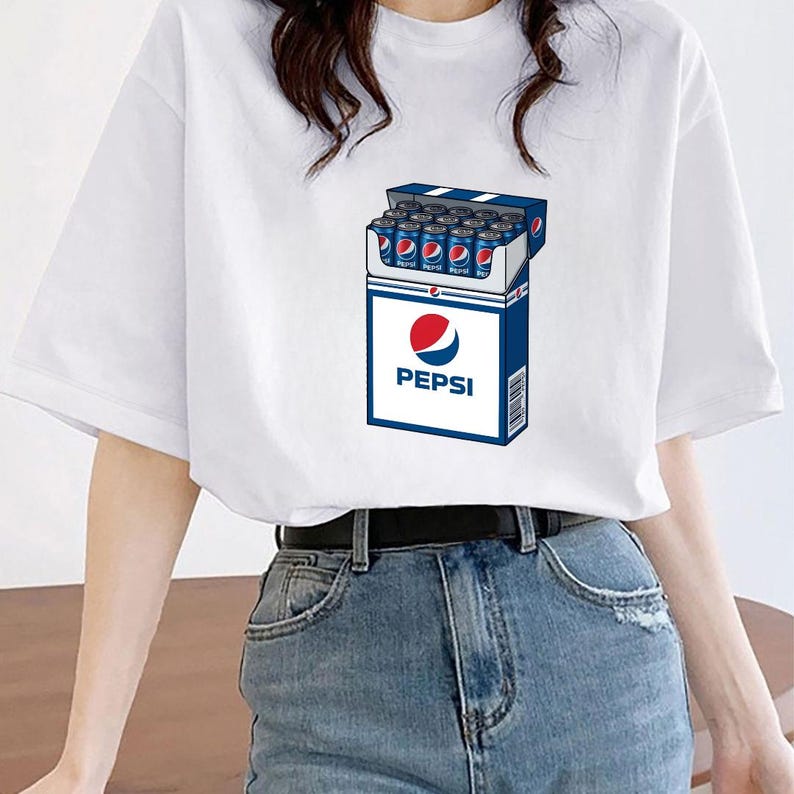 May include: A white short-sleeved t-shirt featuring a graphic print of a blue and white box designed to resemble a cigarette pack, but filled with blue Pepsi soda cans. The Pepsi logo and text are clearly visible on the front of the box graphic.