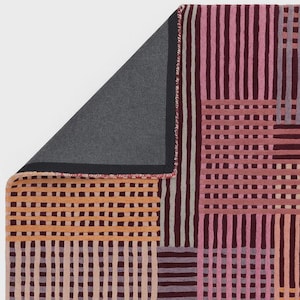 Könnte beinhalten: Ein farbenfroher Teppich mit geometrischem Muster. Der Teppich weist eine Mischung aus Farben auf, darunter Orange, Rosa und Burgunder, die in einem gitterartigen Design angeordnet sind. Die Unterseite des Teppichs ist grau. Die Abmessungen des Teppichs sind nicht sichtbar.