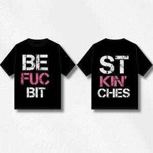 May include: Two black t-shirts with white and pink text. One shirt reads "BE FUC BIT" and the other reads "ST KIN' CHES". The shirts are short-sleeved and have a crew neck.