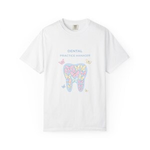 May include: White t-shirt with a round neck featuring a tooth-shaped design filled with pastel butterflies. The text "DENTAL PRACTICE MANAGER" is printed above the tooth graphic in light blue.
