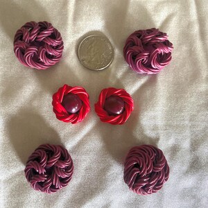 May include: An assortment of handmade earrings in shades of red and purple. The earrings feature a woven design, with some having a central bead. A US quarter is included for size reference. The earrings are displayed on a white, textured surface.