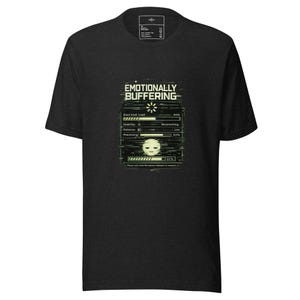 Puede incluir: Camiseta gris oscuro con un gráfico que dice "Emotionally Buffering". El diseño presenta una barra de carga con el texto "Emotional Load", "Stability", "Patience" y "Processing". Una cara triste está en la parte inferior.